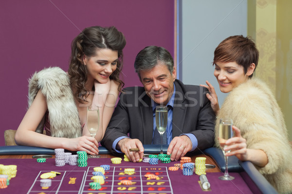 [[stock_photo]]: Homme · deux · femmes · parler · roulette · table · casino