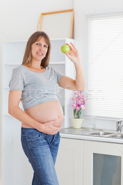 Attractive pregnant woman posing while holding a green apple in a kitchen Stock photo © wavebreak_media