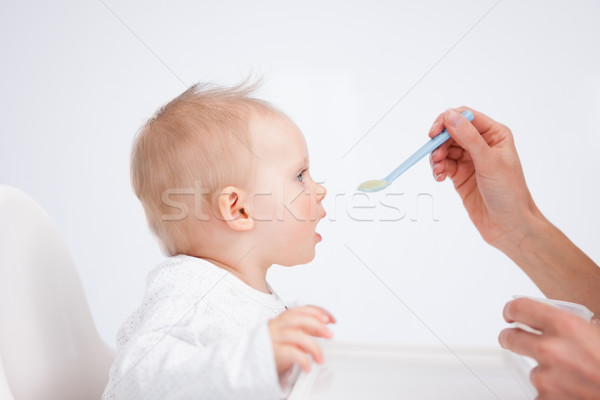 Cute baby sitting on a highchair while being fed against a grey background Stock photo © wavebreak_media