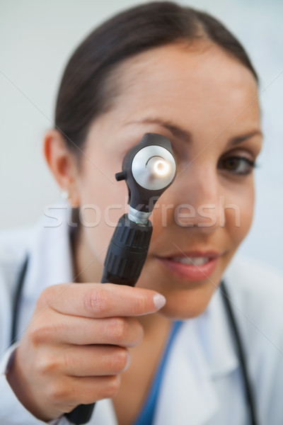 Doctor wearing lab coat looks through otoscope instrument  Stock photo © wavebreak_media
