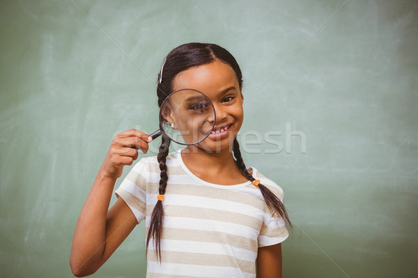 Stock photo: Little girl holding magnifying glass in classroom