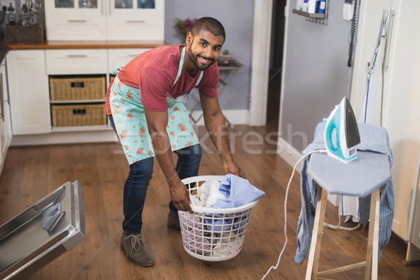 Portrait of smiling man lifting laundry basket by ironing board in kitchen Stock photo © wavebreak_media