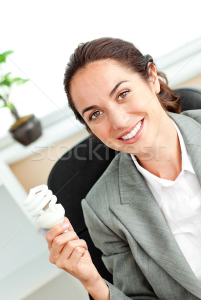 Bright hispanic businesswoman holding a light bulb sitting at her desk in her office Stock photo © wavebreak_media