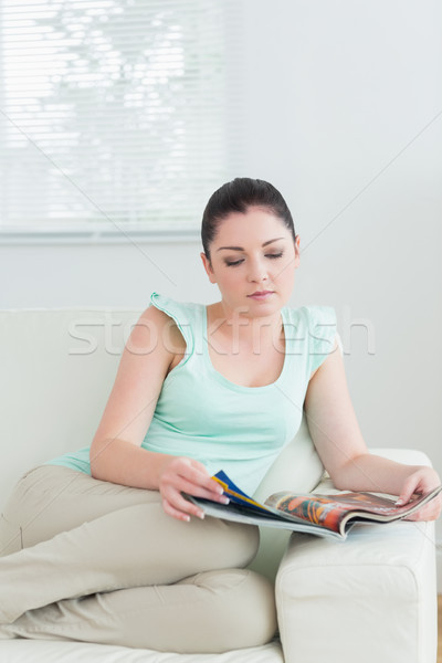 Stock photo: Woman sitting in a living room on a couch and reading a magazine