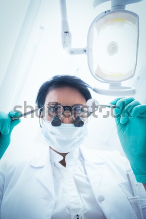 Dentist in surgical mask and dental loupes looking down over pat Stock photo © wavebreak_media