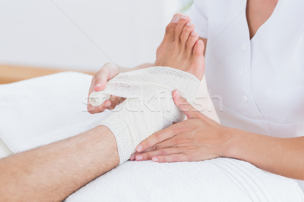 Stock photo: Doctor bandaging her patient ankle 