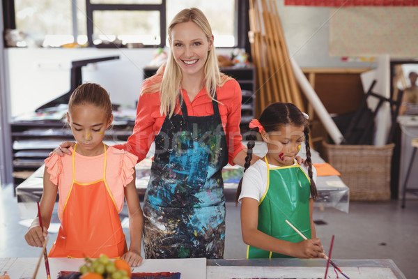 Stock photo: smiling teacher standing with schoolkids in drawing class