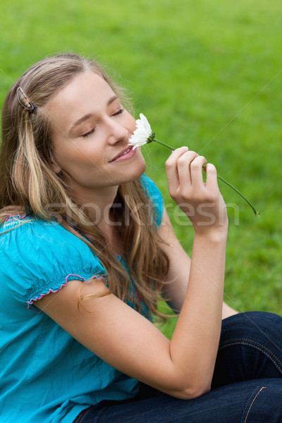 Stock photo: Young happy woman closing her eyes while sitting on the grass and smelling a flower