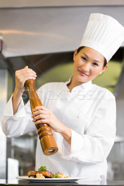 Smiling female cook grinding pepper on food in kitchen Stock photo © wavebreak_media