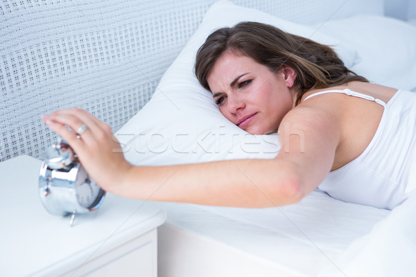 Pretty woman extending hand to alarm clock in bed  Stock photo © wavebreak_media