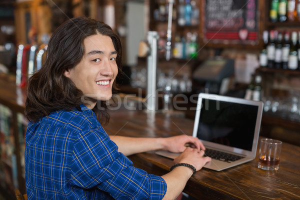 Stock photo: Smiling young man using laptop at bar counter