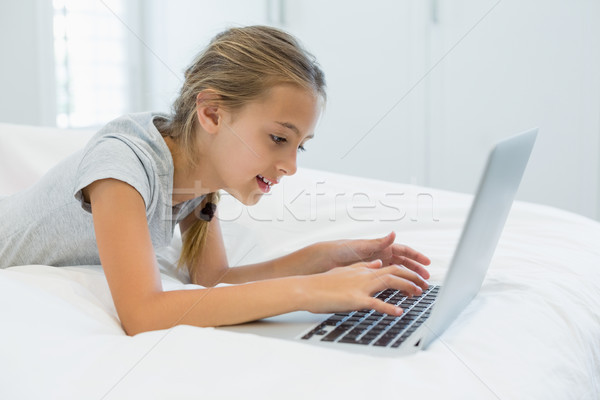 Smiling girl lying on bed and using laptop in bedroom Stock photo © wavebreak_media