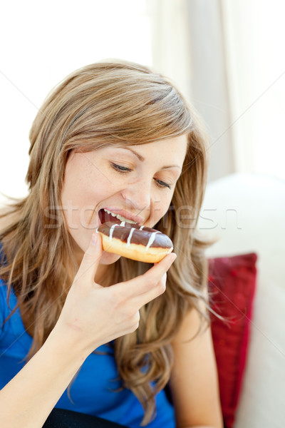 Radiant woman is eating a donut on a sofa  Stock photo © wavebreak_media