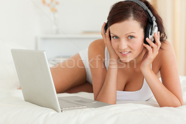 Woman listening to music working on a laptop looking at the camera in the bedroom Stock photo © wavebreak_media
