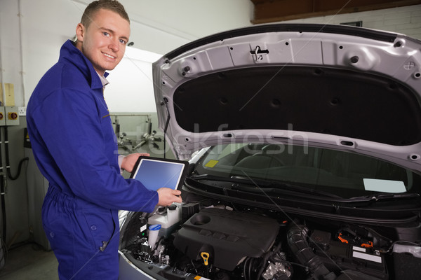 Stock photo: Mechanic looking at camera while holding a tablet computer in a garage