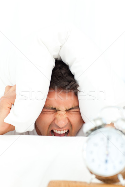 Man stressed by his alarm clock putting his head under the pillow in the bedroom  Stock photo © wavebreak_media
