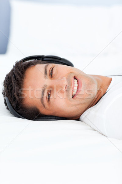 Stock photo: Cheerful man listening music with headphones lying on his bed at home