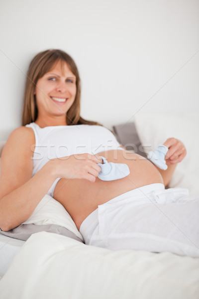 Charming pregnant woman playing with little socks while lying on a bed in her apartment Stock photo © wavebreak_media