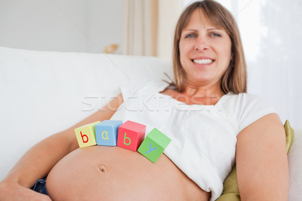 Pretty pregnant female playing with wooden blocks while lying on a sofa in her living room Stock photo © wavebreak_media
