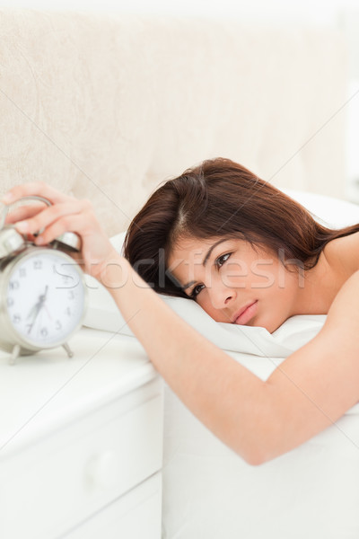 Stock photo: A woman is lying on her bed, now awake, she has her hand on the alarm clock to silence the ringing.