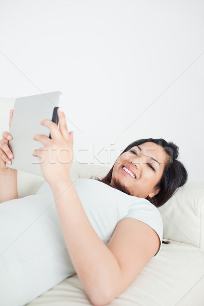 Smiling woman lying on a sofa while holding a tactile tablet in a living room Stock photo © wavebreak_media