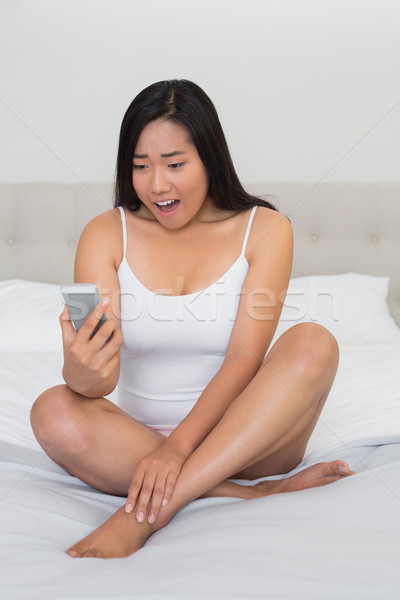 Shocked woman sitting on bed reading a text  Stock photo © wavebreak_media