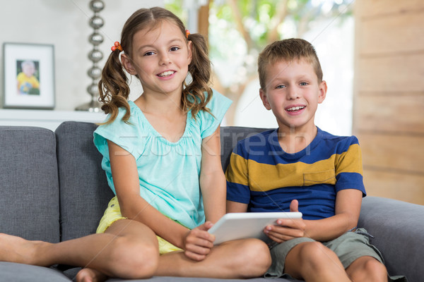 Portrait of siblings with digital tablet sitting on sofa in living room Stock photo © wavebreak_media