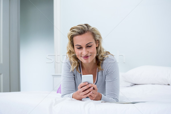 Smiling woman using phone while lying on bed Stock photo © wavebreak_media