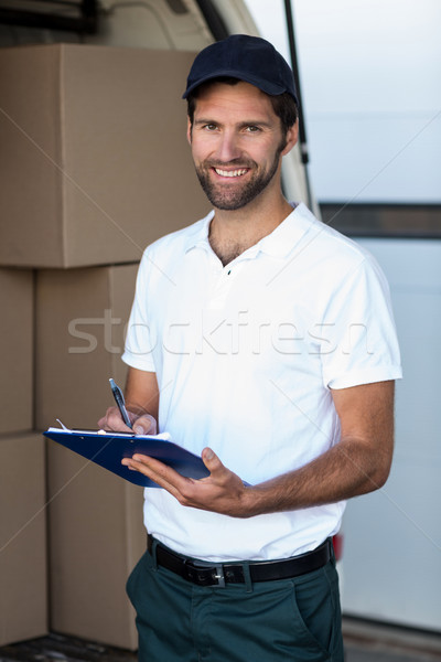 Stock photo: Delivery man writing on clipboard while standing next to his van
