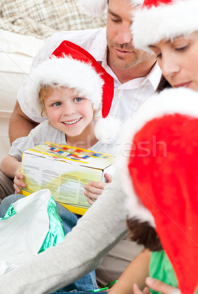 Happy boy holding a christmas gift sitting on the floor with his family  Stock photo © wavebreak_media