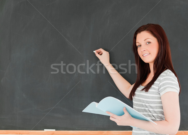 [[stock_photo]]: Jeune · femme · écrire · tableau · noir · regarder · caméra · classe