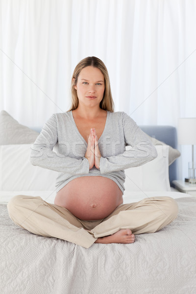 Stock photo: Serious pregnant woman doing yoga sitting on the bed