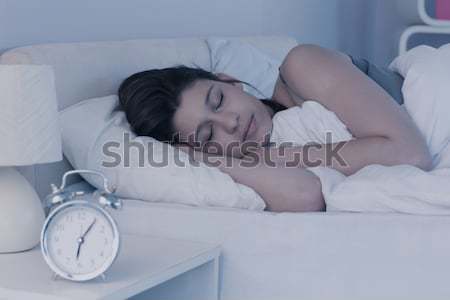 Tired woman hidding her head in a pillow while the alarmclock is ringing in her bedroom Stock photo © wavebreak_media