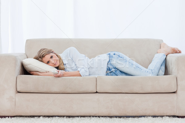 A woman holding a TV remote control is lying on a couch resting her head on a pillow  Stock photo © wavebreak_media