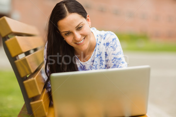 Smiling brunette lying on bench using laptop Stock photo © wavebreak_media