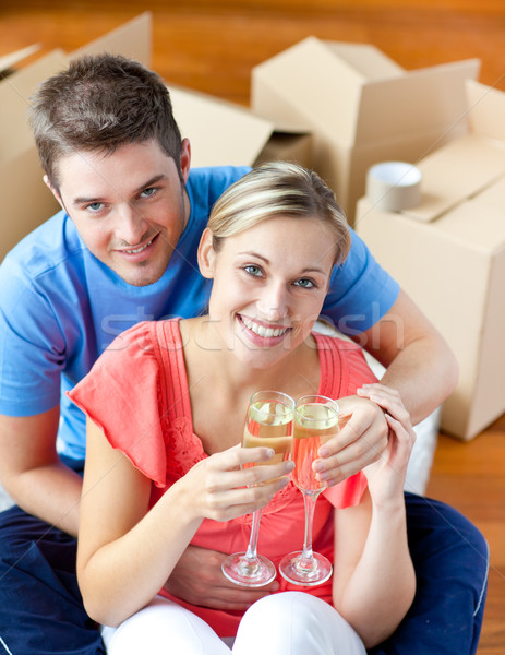 Stock photo: cheerful couple celebrating their new house with champagne sitting on the floor looking at the camer