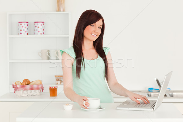 Stock photo: Good looking red-haired female relaxing with her laptop in the kitchen in her appartment