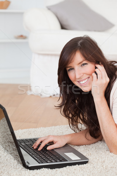 Stock photo: Cute brunette woman on the phone while relaxing with her laptop in the living room