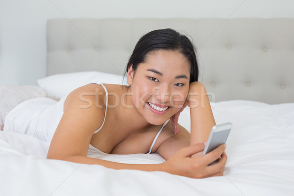 Smiling asian woman lying on bed sending a text Stock photo © wavebreak_media
