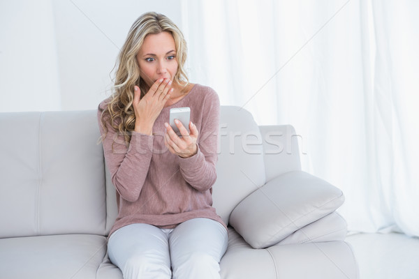 Surprised blonde sitting on couch reading message  Stock photo © wavebreak_media