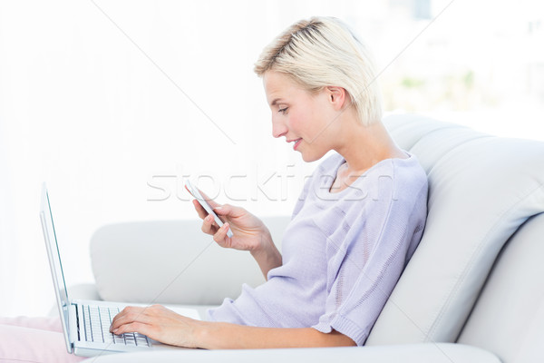 Stock photo: Pretty blonde woman texting with her mobile phone and using her 