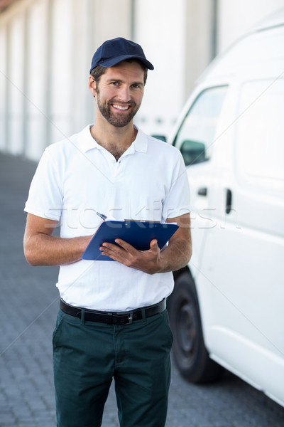 Portrait of delivery man is holding a clipboard and smiling to t Stock photo © wavebreak_media