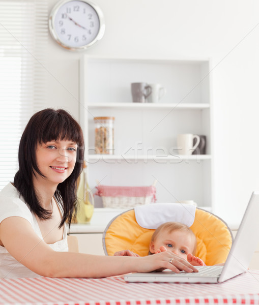 Good looking brunette woman relaxing with her laptop next to her baby while sitting in the kitchen Stock photo © wavebreak_media
