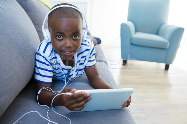 Stock photo: High angle portrait of boy using digital tablet while listening to headphones on sofa at home