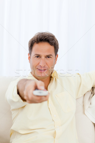 Relaxed man pointing a remote to the camera while relaxing on the sofa Stock photo © wavebreak_media