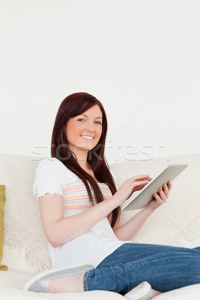 Stock photo: Attractive red-haired woman relaxing with her tablet while sitting on a sofa in the living room