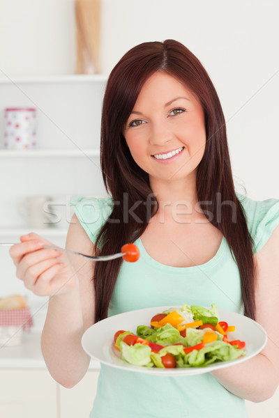 Stock photo: Good looking red-haired woman enjoying a mixed salad in the kitchen in her appartment