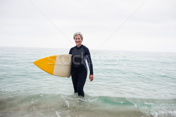 Senior woman in wetsuit standing in water with surfboard on the  Stock photo © wavebreak_media