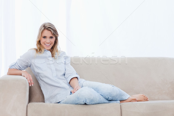 Stock photo: A blonde smiling woman sitting on a couch is looking at the camera