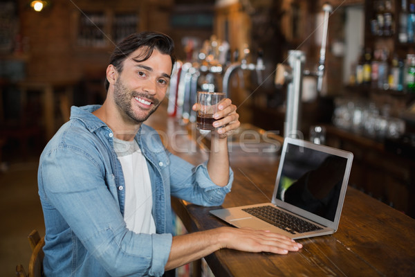 Young man holding beer while sitting by laptop in pub Stock photo © wavebreak_media